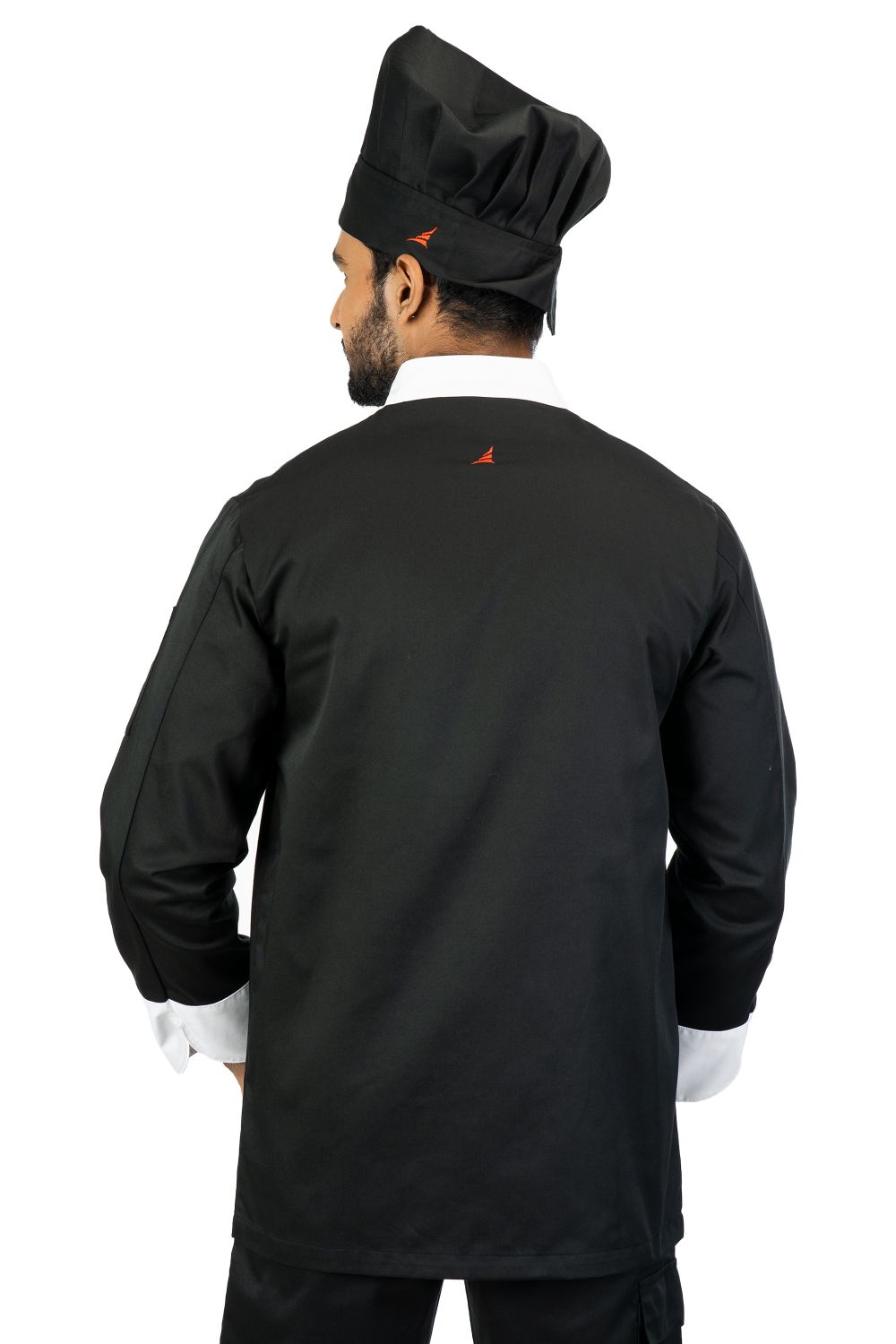 Man wearing black chef jacket with white collar and cuffs, and matching black chef hat, back view