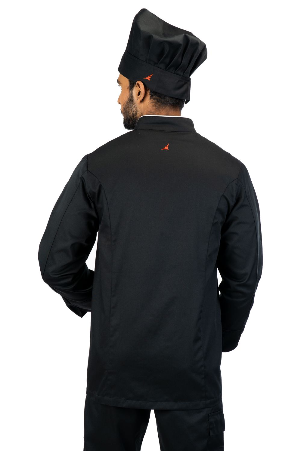 Man wearing all-black chef jacket and matching chef hat, back view, with small orange logo on jacket and hat band