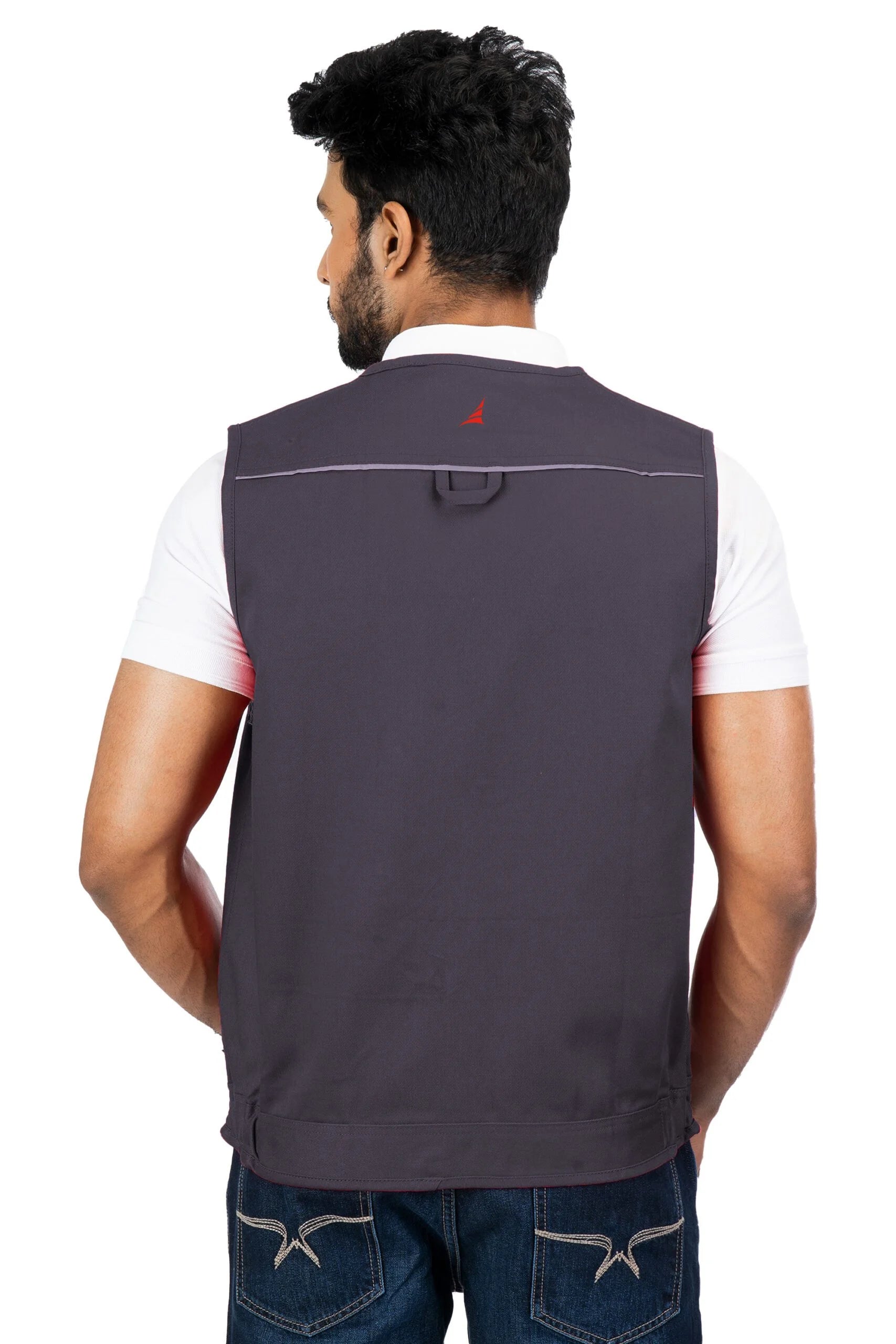 Man wearing dark gray multi-utility vest with reflective piping and red logo on back over white shirt, rear view
