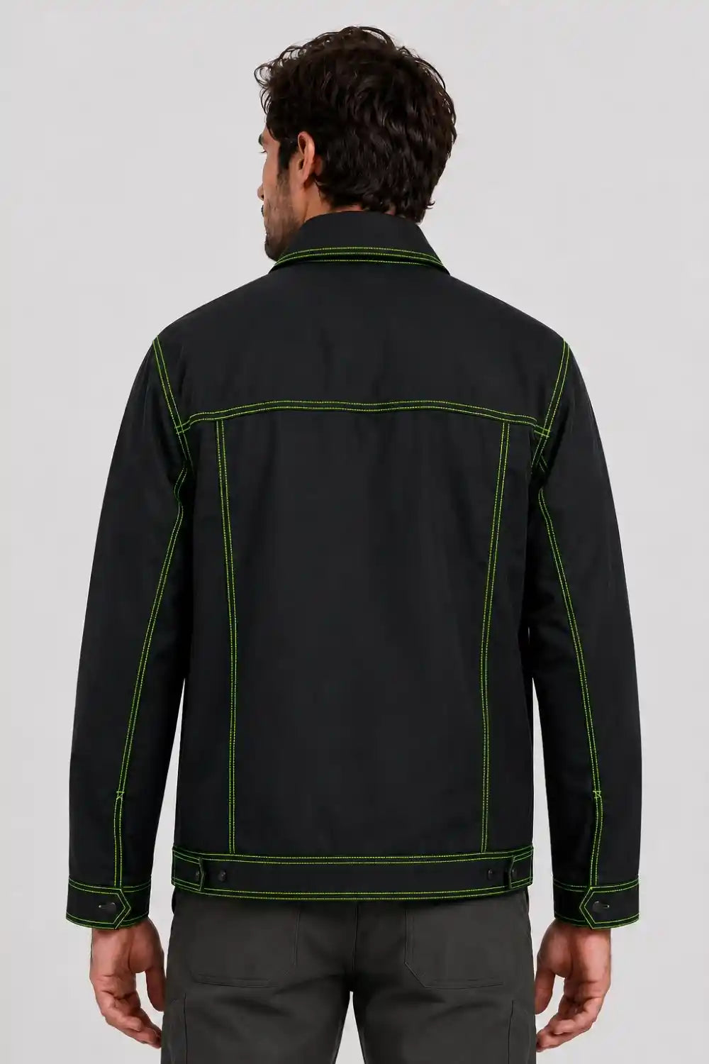A man viewed from the back wearing a black jacket with bright green contrast stitching, paired with dark gray trousers, against a light gray studio background.