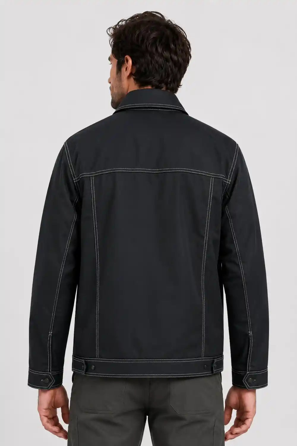 A man viewed from the back wearing a black jacket with contrasting light stitching and dark gray pants, set against a plain light gray studio background.