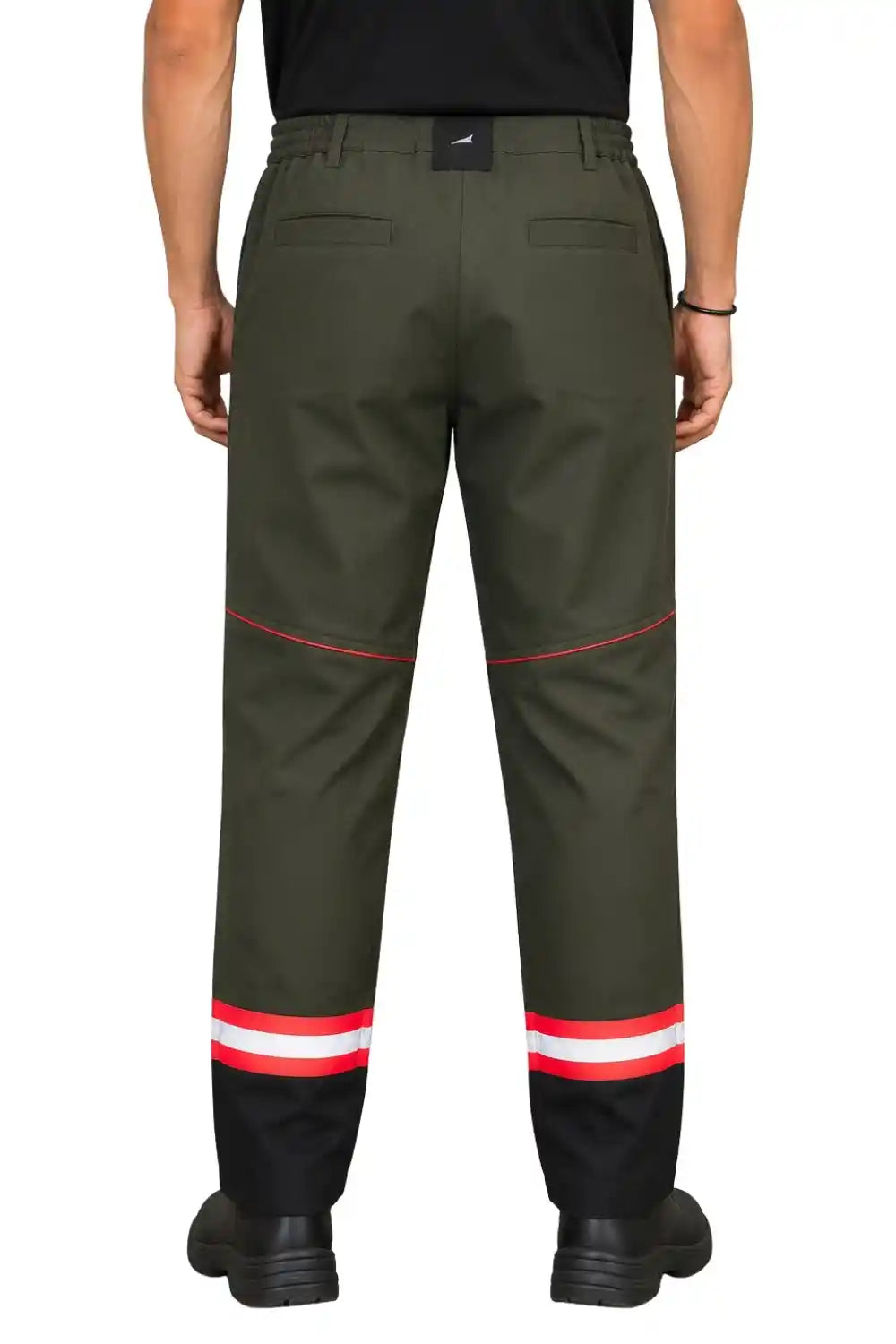 A person shown from the back wearing dark olive green work pants with red piping and reflective red, white, and black striped cuffs, from atacamapro.com, paired with a black shirt and black boots on a white background.